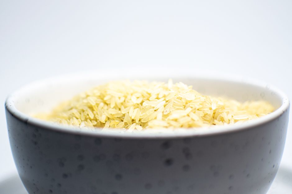 A close-up view of uncooked white rice in a speckled ceramic bowl on a light background.