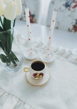 A styled coffee scene with a floral cup, tulips, and decorated candles.