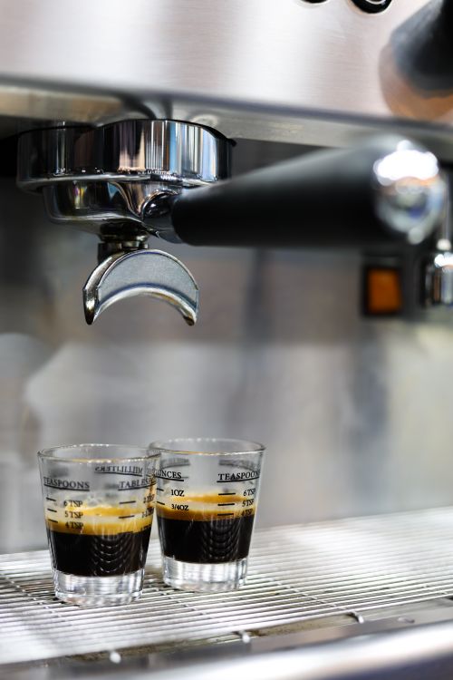 Free Close-up of two fresh espresso shots being brewed from a stainless steel espresso machine in a cafe setting. Stock Photo