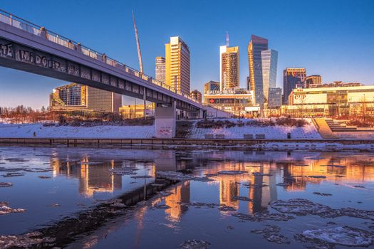Urban cityscape with modern high-rise buildings reflecting on the river during daytime.