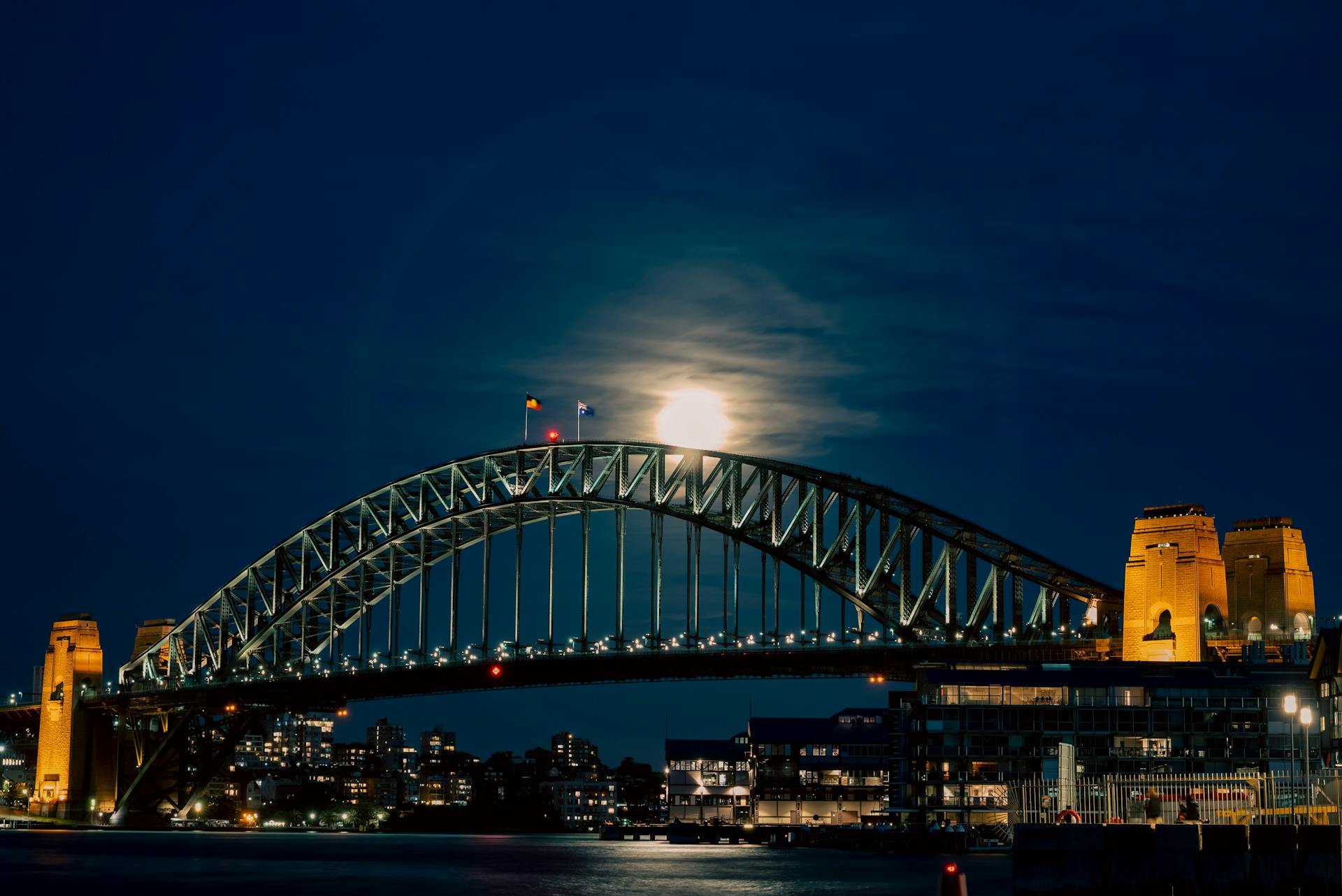 Dramatic view of Sydney Harbour Bridge illuminated by moonlight over Sydney's skyline at night.