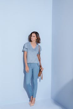Chic woman posing in a monochromatic blue outfit against a light blue background, holding a brown handbag.