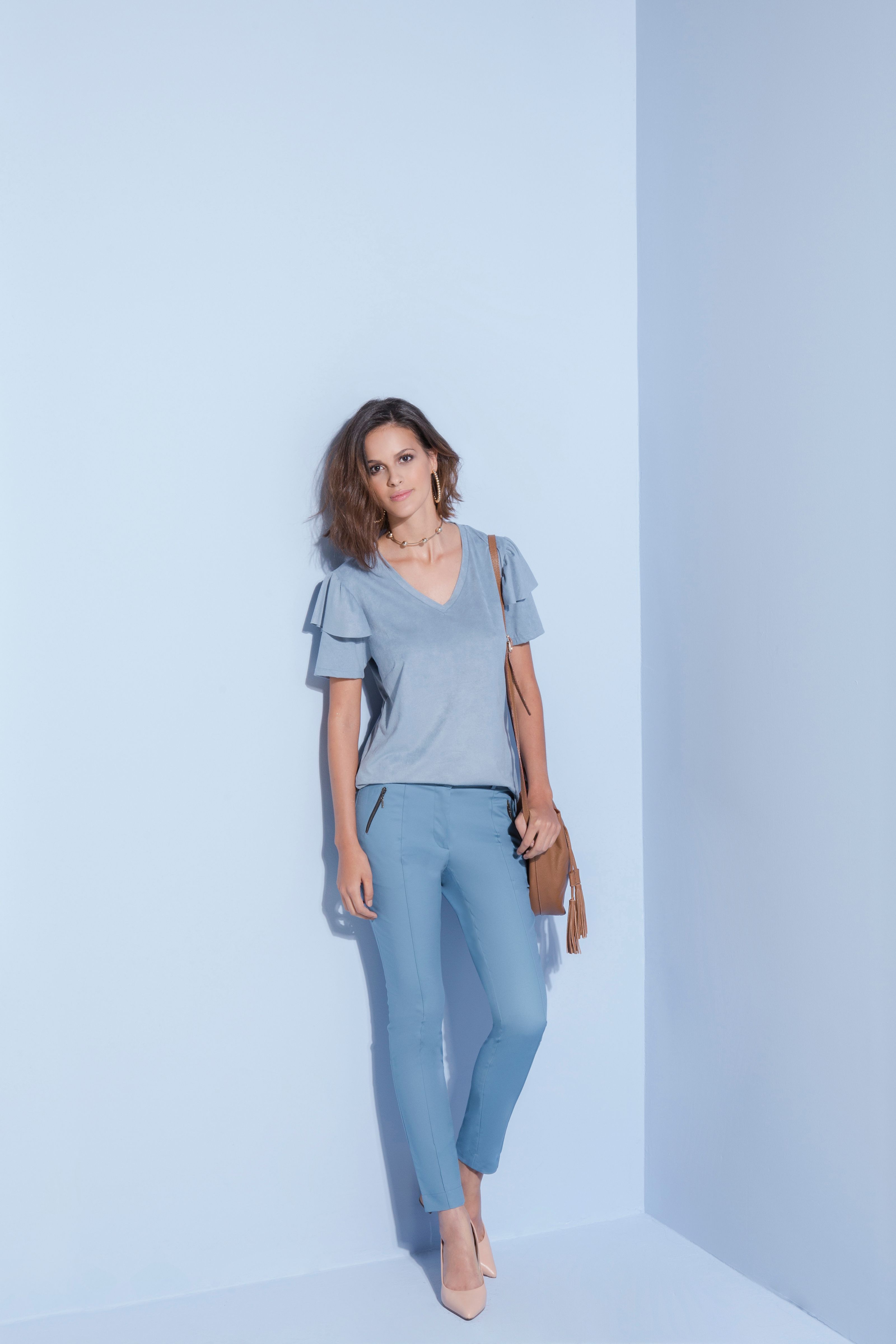 Mulher em elegante traje azul posando em um cenário minimalista, oferecendo inspiração de moda.
