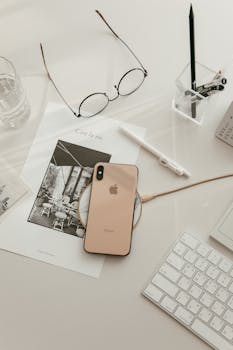 Modern minimalist workspace setup featuring smartphone, keyboard, glasses, and stationery.