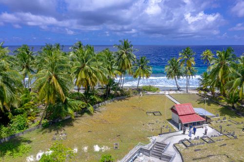 Free Aerial view of a tropical beach with palm trees, turquoise ocean, and a small building. Ideal for travel and nature themes. Stock Photo