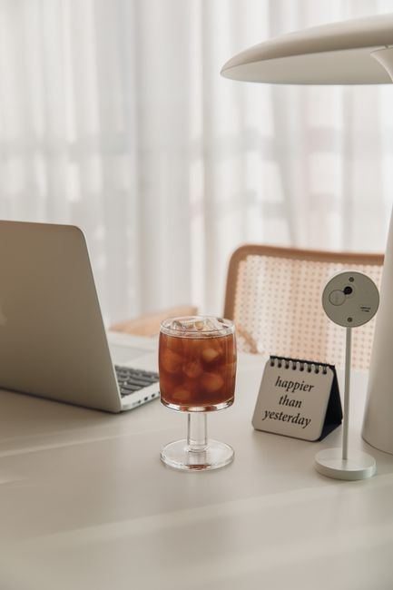 Cozy workspace featuring a laptop, iced coffee, and motivational note in soft lighting.