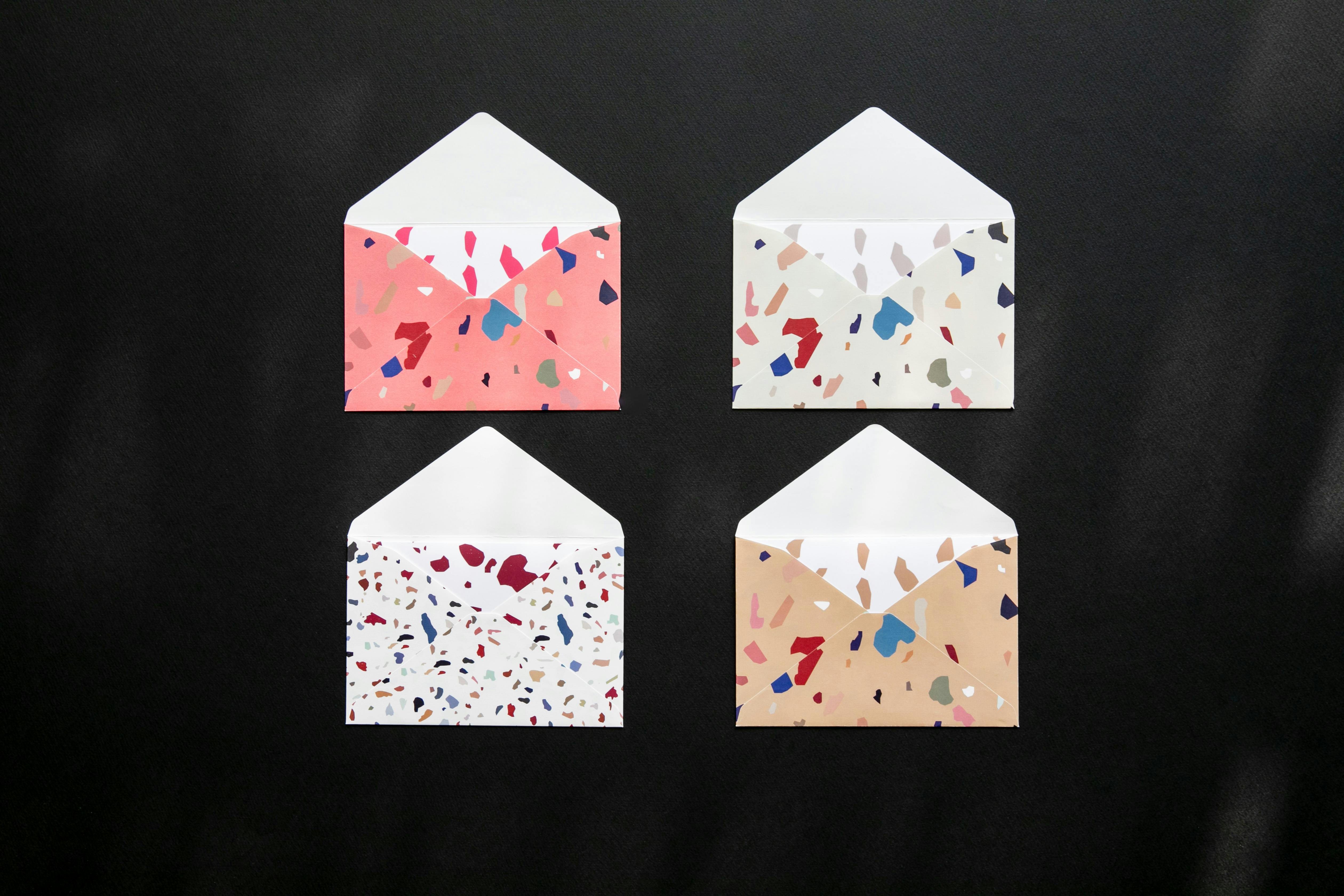 무료 검은색 표면에 다채로운 테라조 디자인이 들어간 4개의 패턴 봉투입니다. 스톡 사진