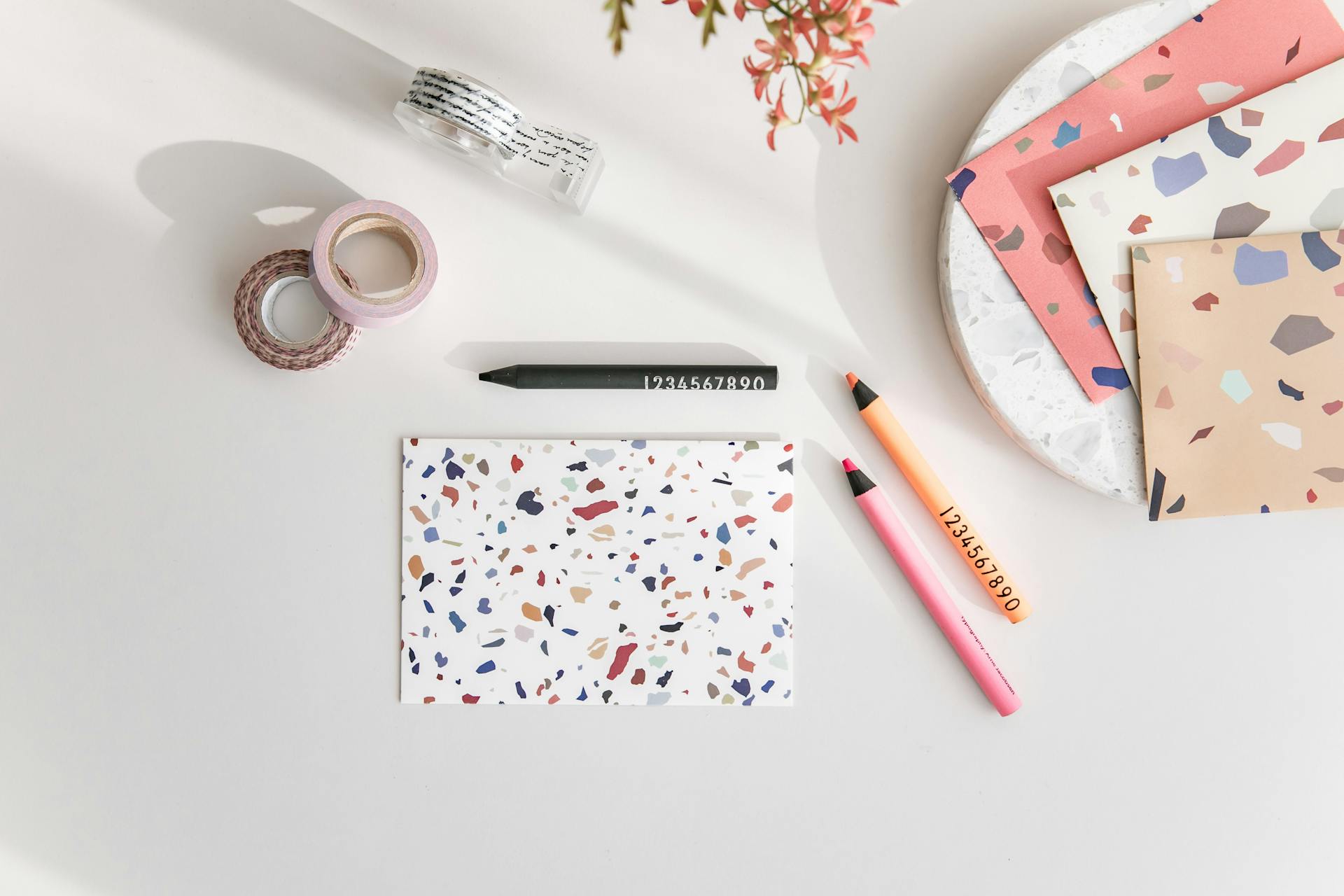 Aerial view of a terrazzo notebook, colorful pencils, and washi tape on a desk.