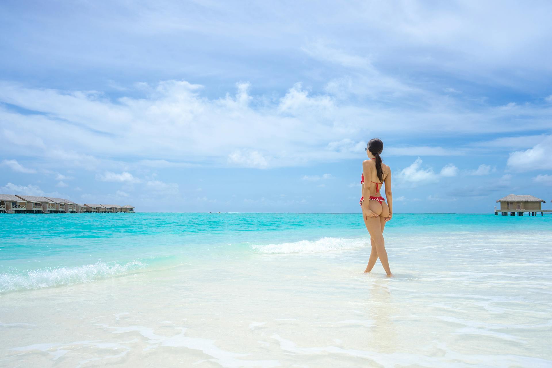 A woman in a bikini enjoys a sunlit day at a tropical beach with clear turquoise waters and bright skies.