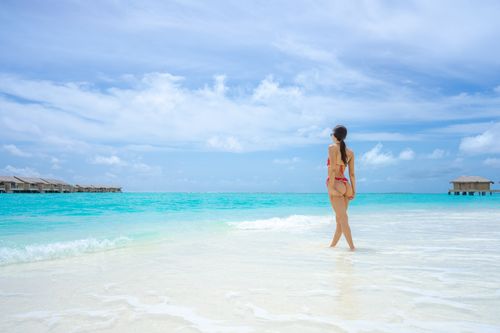 Free A woman in a bikini enjoys a sunlit day at a tropical beach with clear turquoise waters and bright skies. Stock Photo