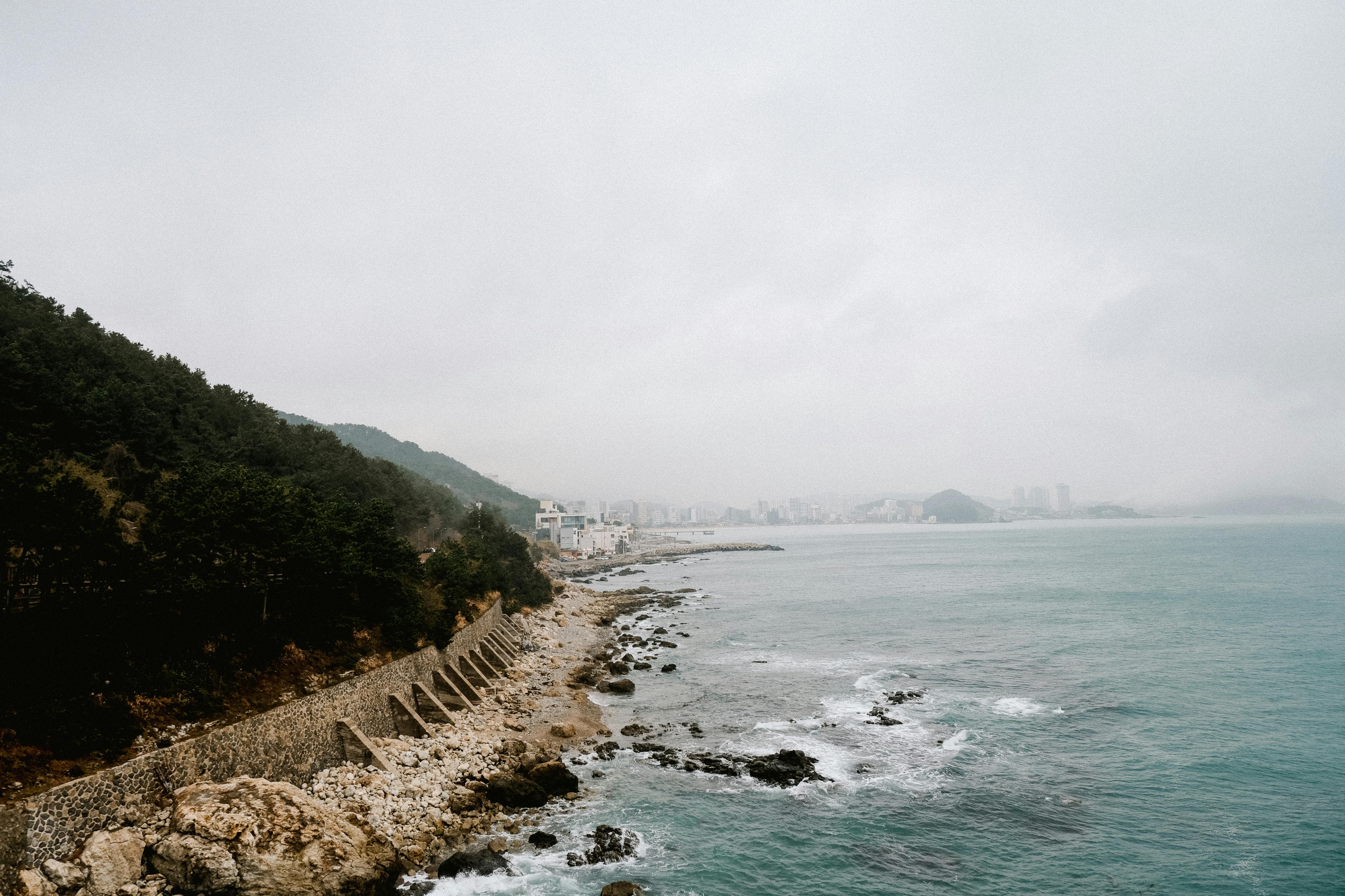 Scenic view of a rocky coastline leading to a distant city under cloudy skies.