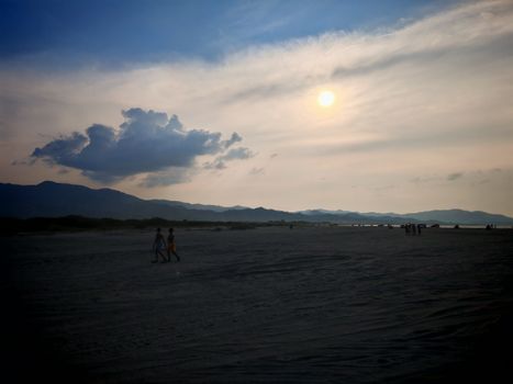 Sunset over a tranquil beach landscape with dramatic clouds and silhouettes of people.