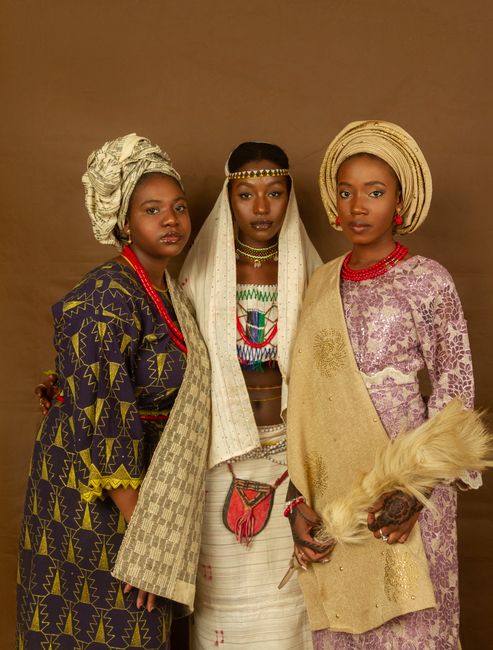 Three women wearing colorful, traditional outfits posing against a brown backdrop.