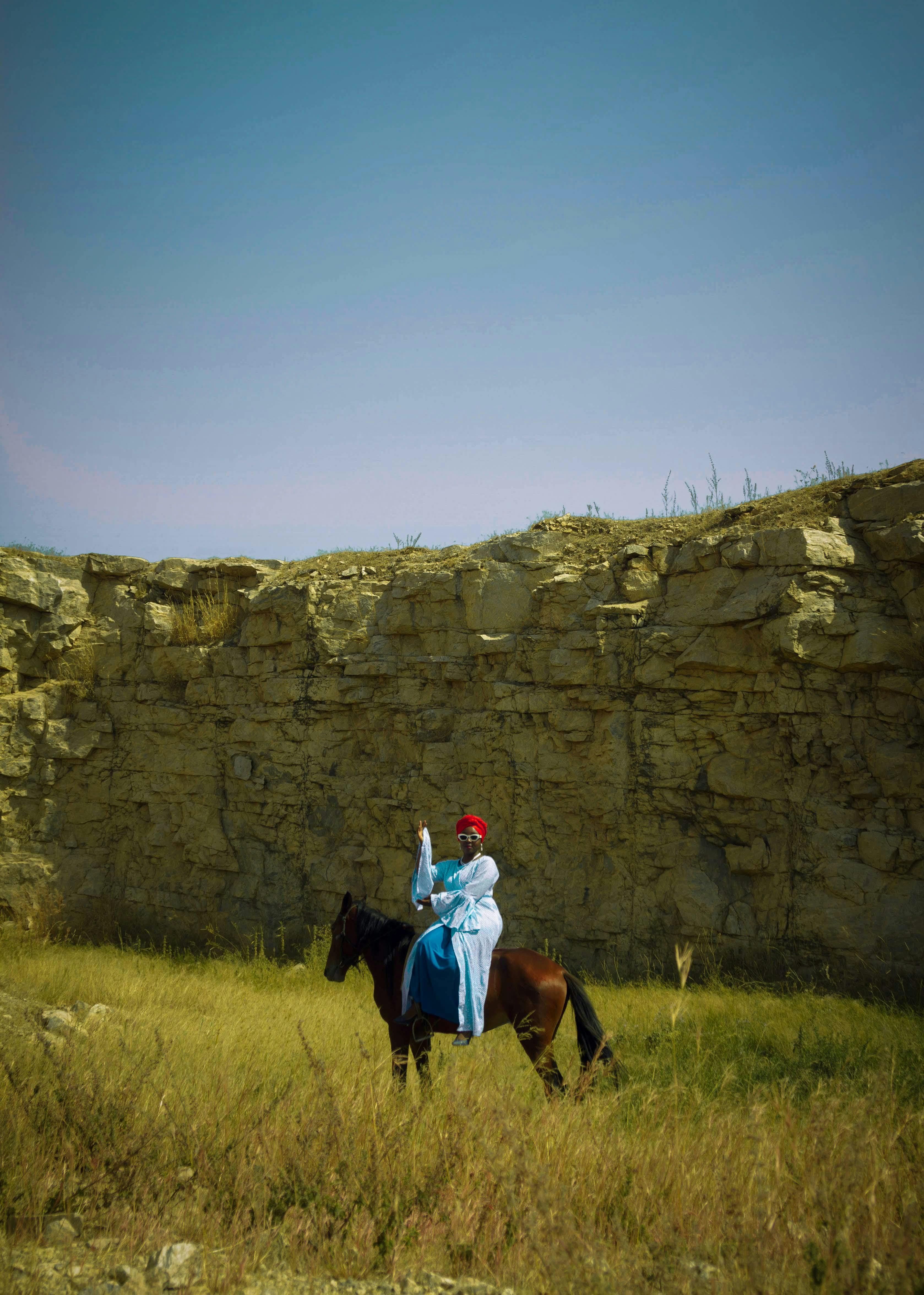 A person in traditional attire rides a horse against a stone cliff backdrop.