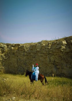 A person in traditional attire rides a horse against a stone cliff backdrop.