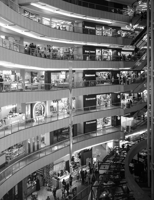 Free Elegant black and white image of a bustling Jakarta shopping mall interior showcasing multiple levels and visible shops. Stock Photo