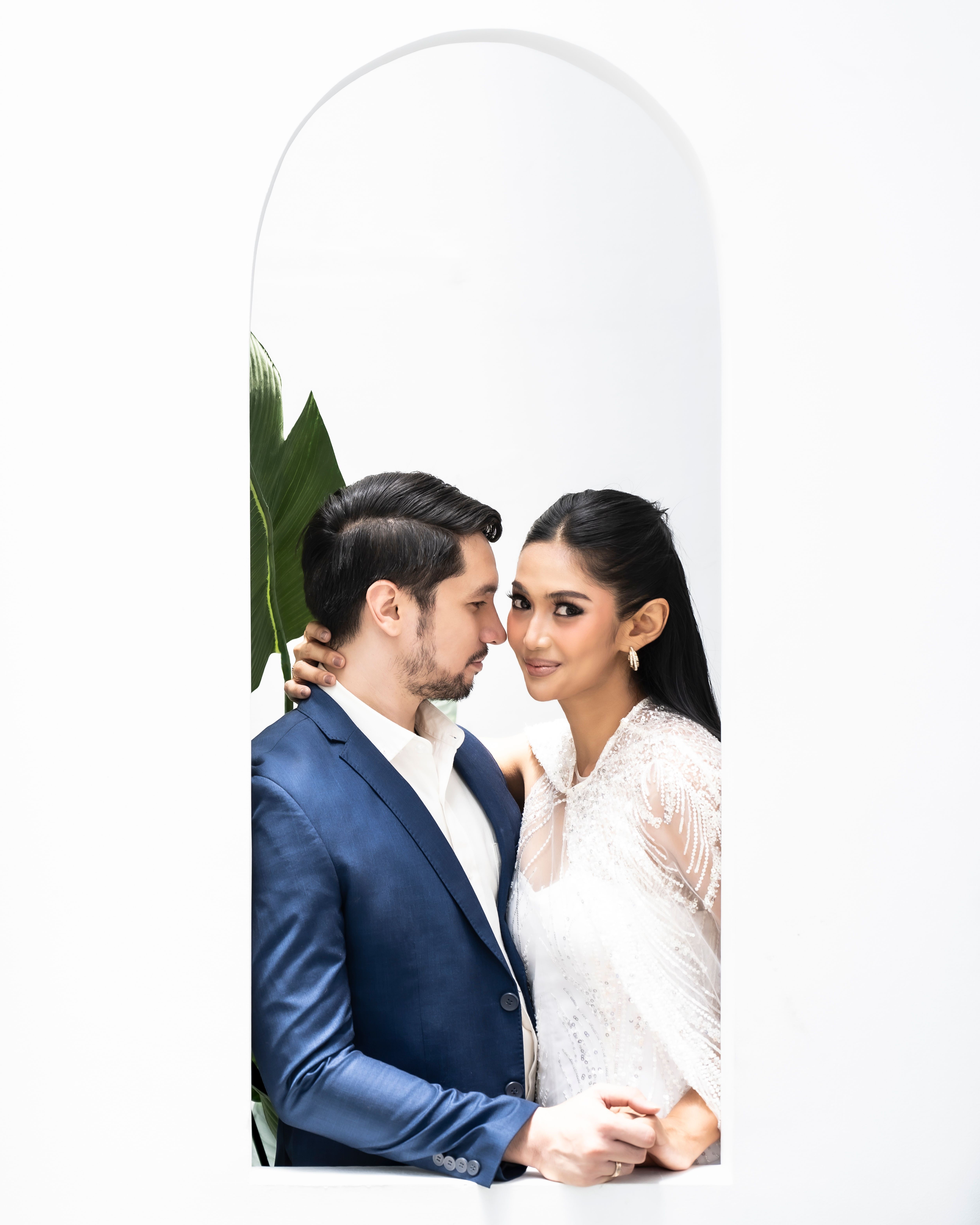 Stylish couple in elegant attire posing gracefully in a bright, minimalist archway setting.