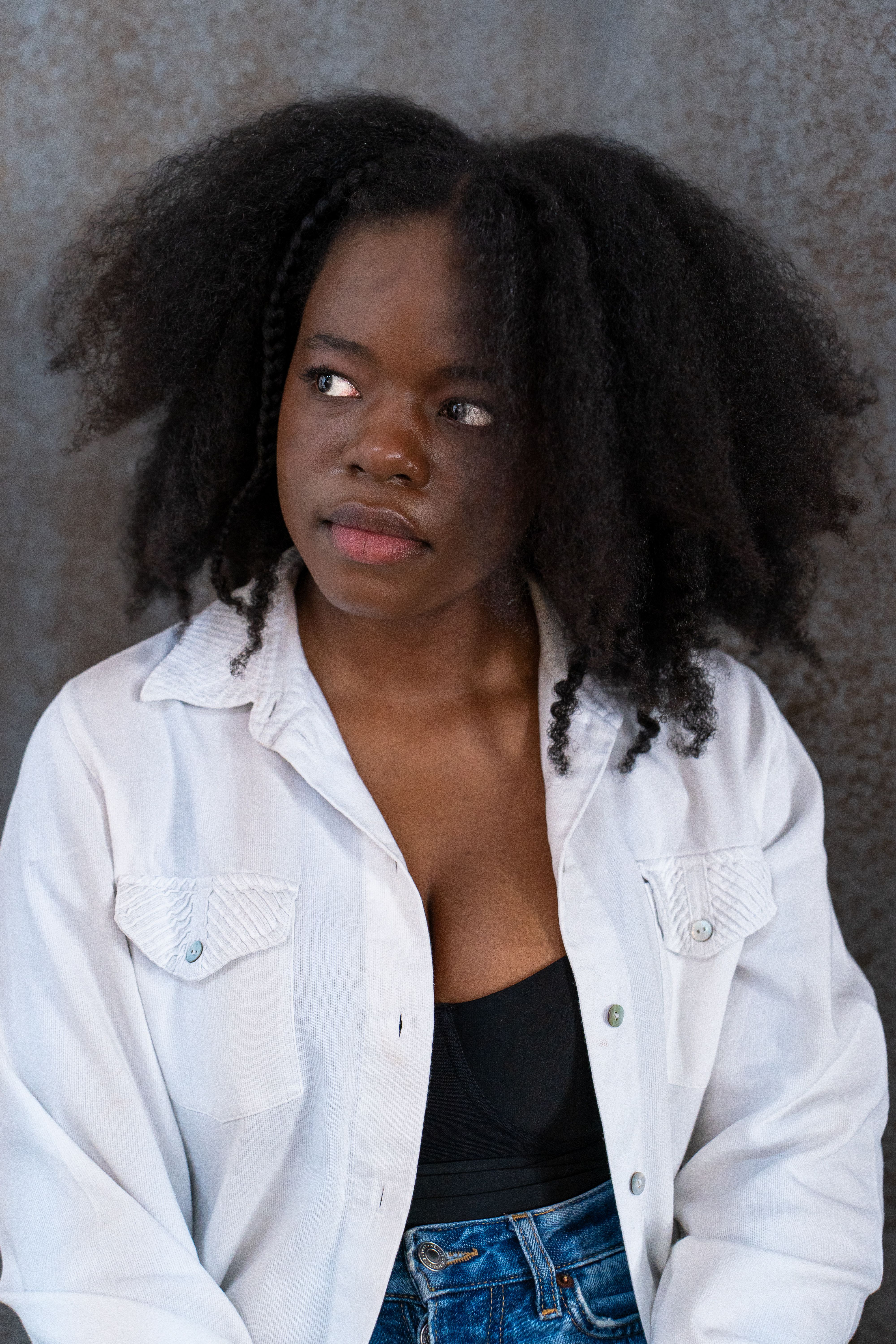 Confident woman with curly hair wearing a white shirt and denim, posing thoughtfully.