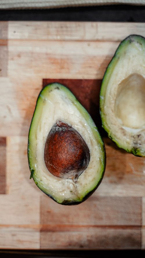 Free Fresh avocado sliced open on a wooden board, highlighting its seed and creamy texture. Stock Photo