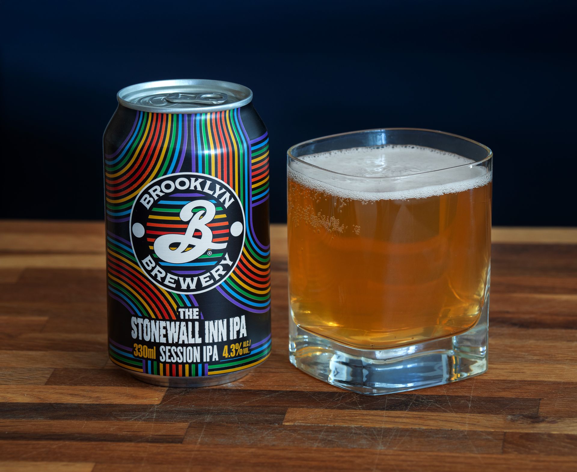 Colorful can of Brooklyn Brewery Stonewall Inn IPA with a glass on a wooden surface.