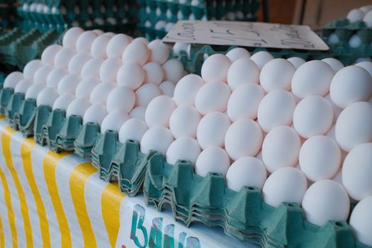 Stacks of fresh white eggs on a green carton tray at a local market. Ideal for culinary themes.