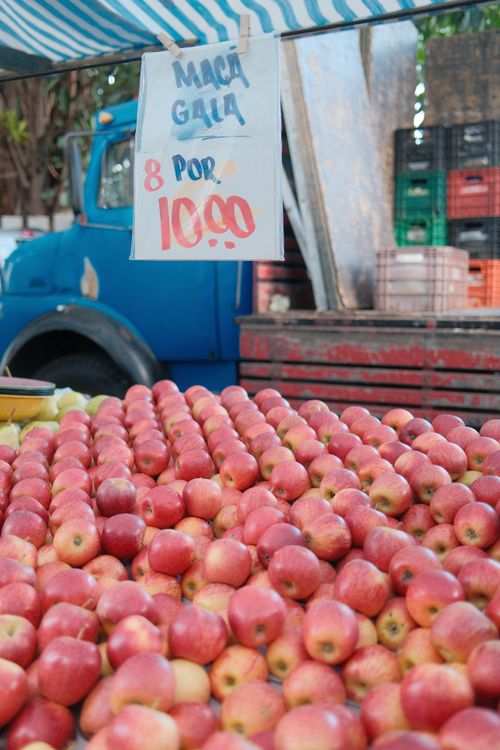 Free Fresh red Gala apples displayed at a market stall with a vintage truck backdrop. Stock Photo