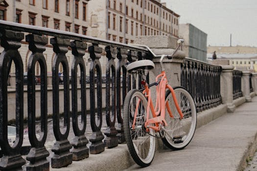 A classic orange bicycle leans against a historic iron railing on a city bridge.