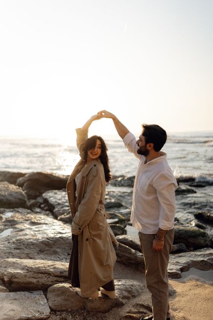Romantic couple dancing on a rocky beach during sunset, exuding love and happiness.