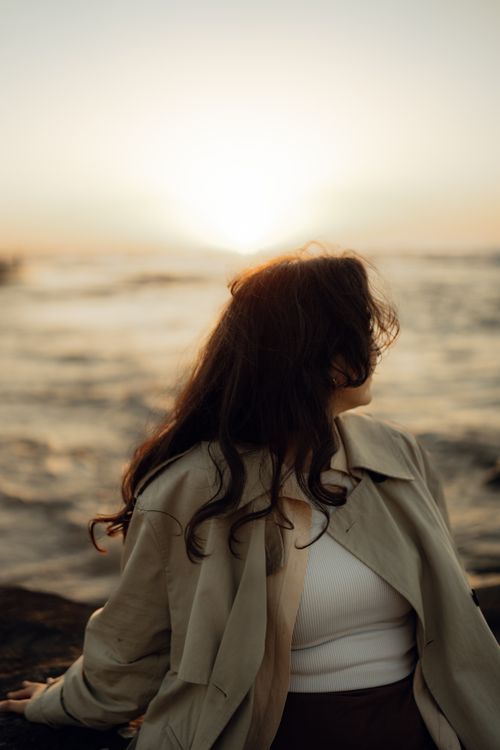 Free A woman looks at the ocean sunset, creating a peaceful and contemplative mood. Stock Photo