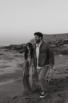 A joyful couple walking along a rocky shoreline at dusk, exuding happiness.