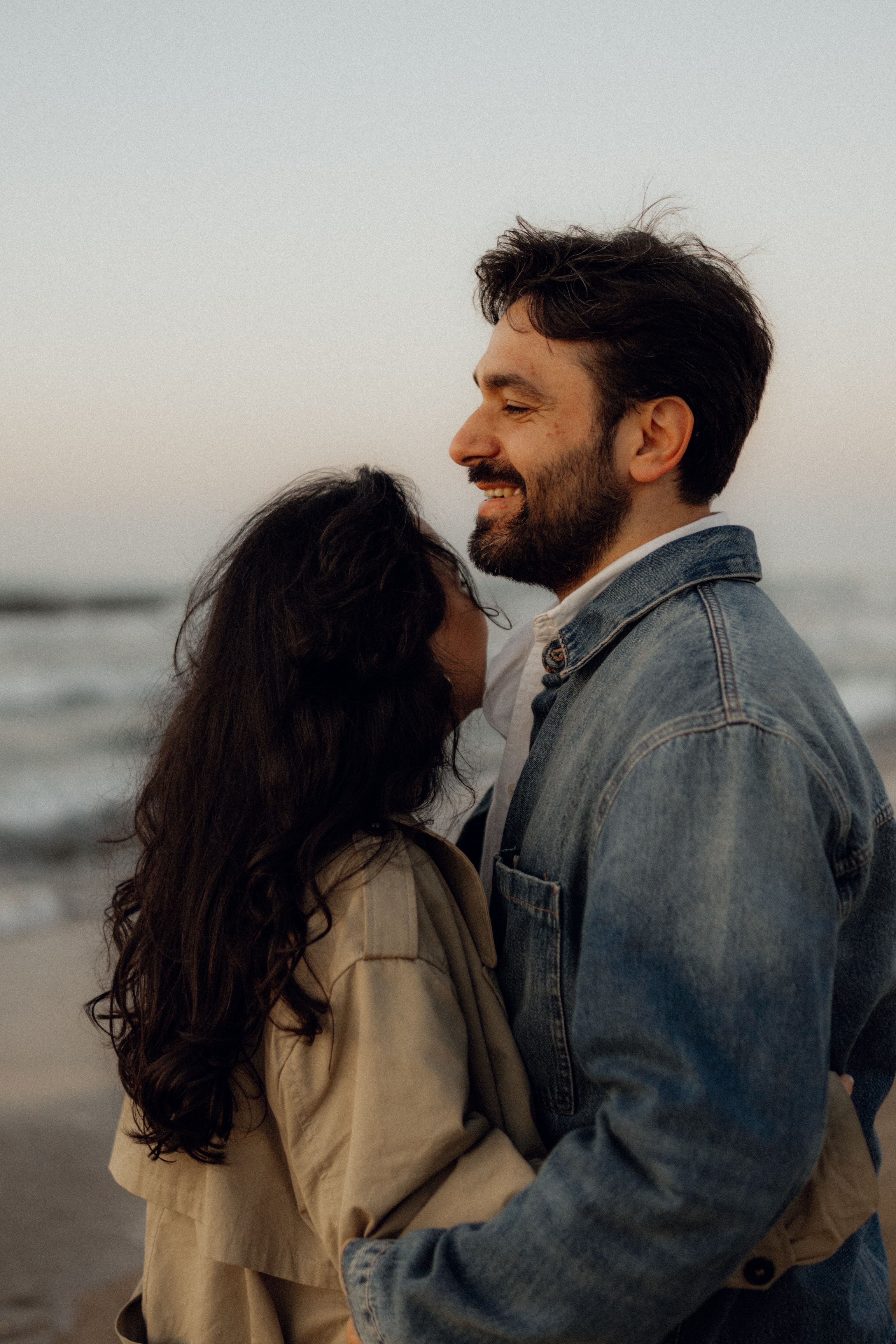 A couple embraces on a beach at sunset, capturing a moment of tenderness and joy.