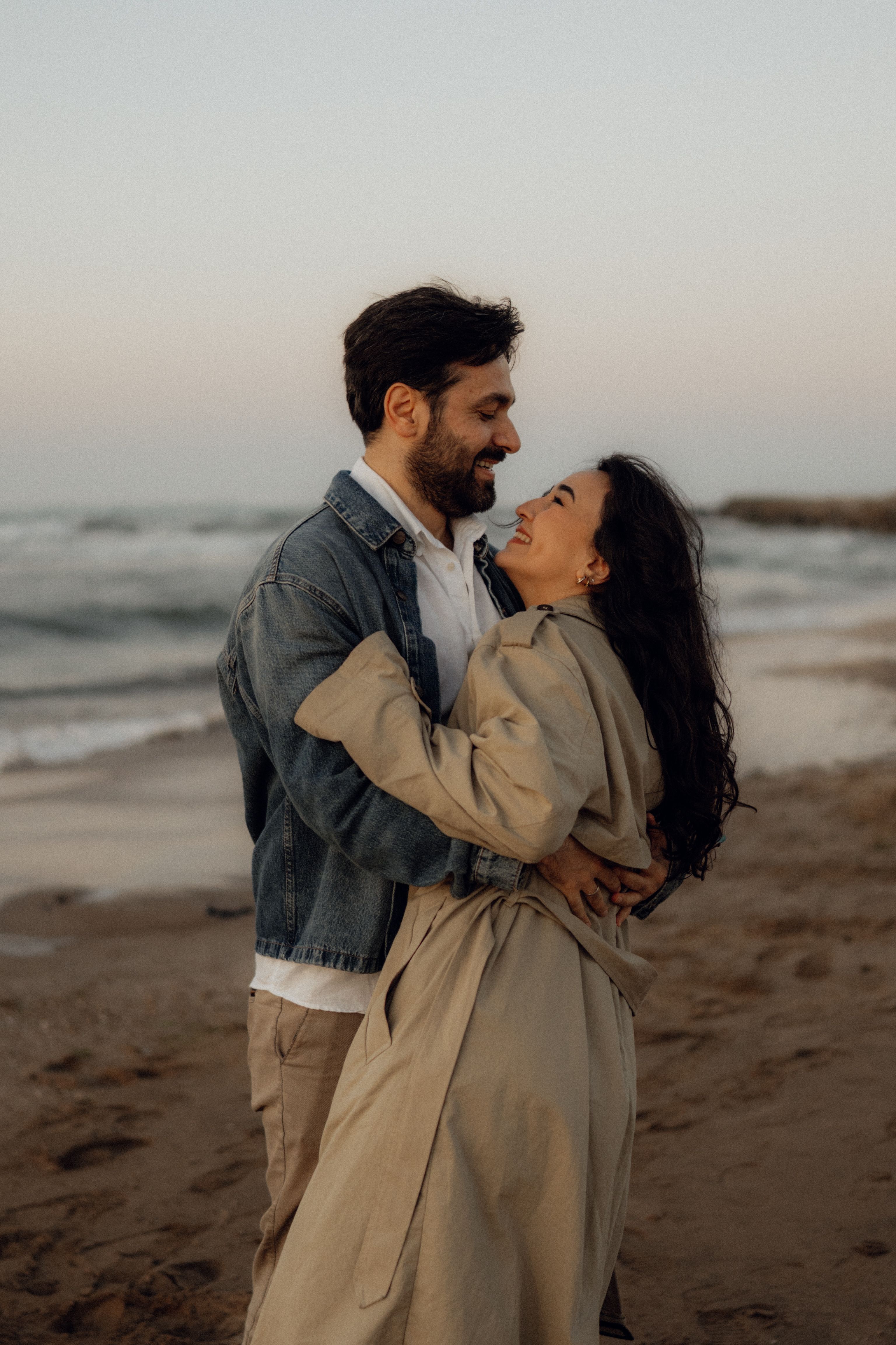 A couple shares a loving embrace on a sandy beach at sunset, capturing a warm moment by the ocean.