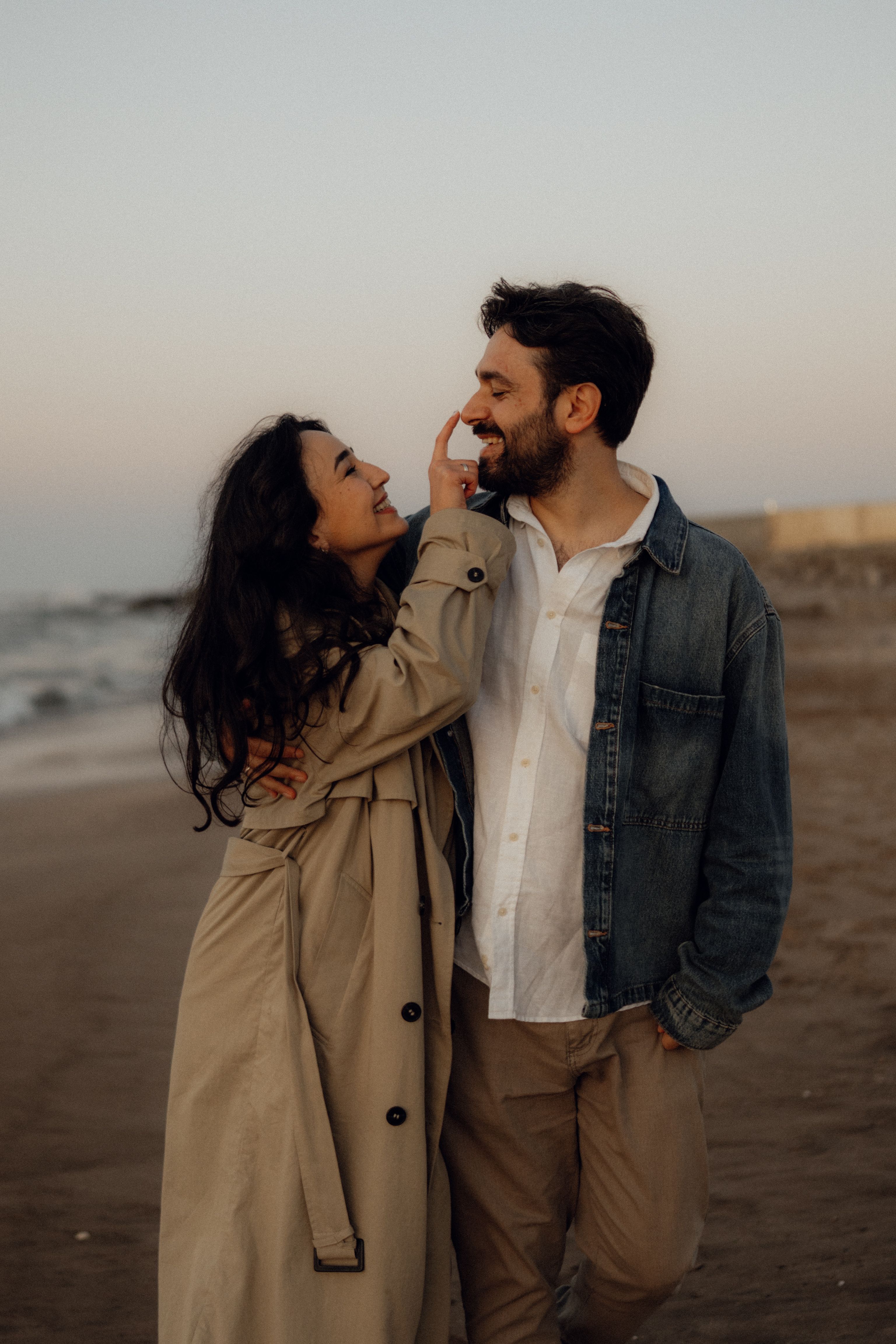 Smiling couple enjoys a romantic walk on the beach during sunset, creating a warm and intimate atmosphere.