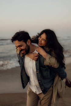 A happy couple shares a playful piggyback ride on the beach during sunset.