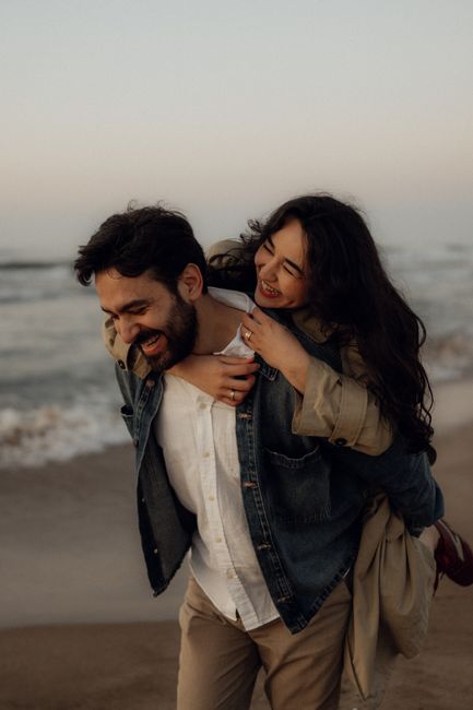 A happy couple shares a playful piggyback ride on the beach during sunset.