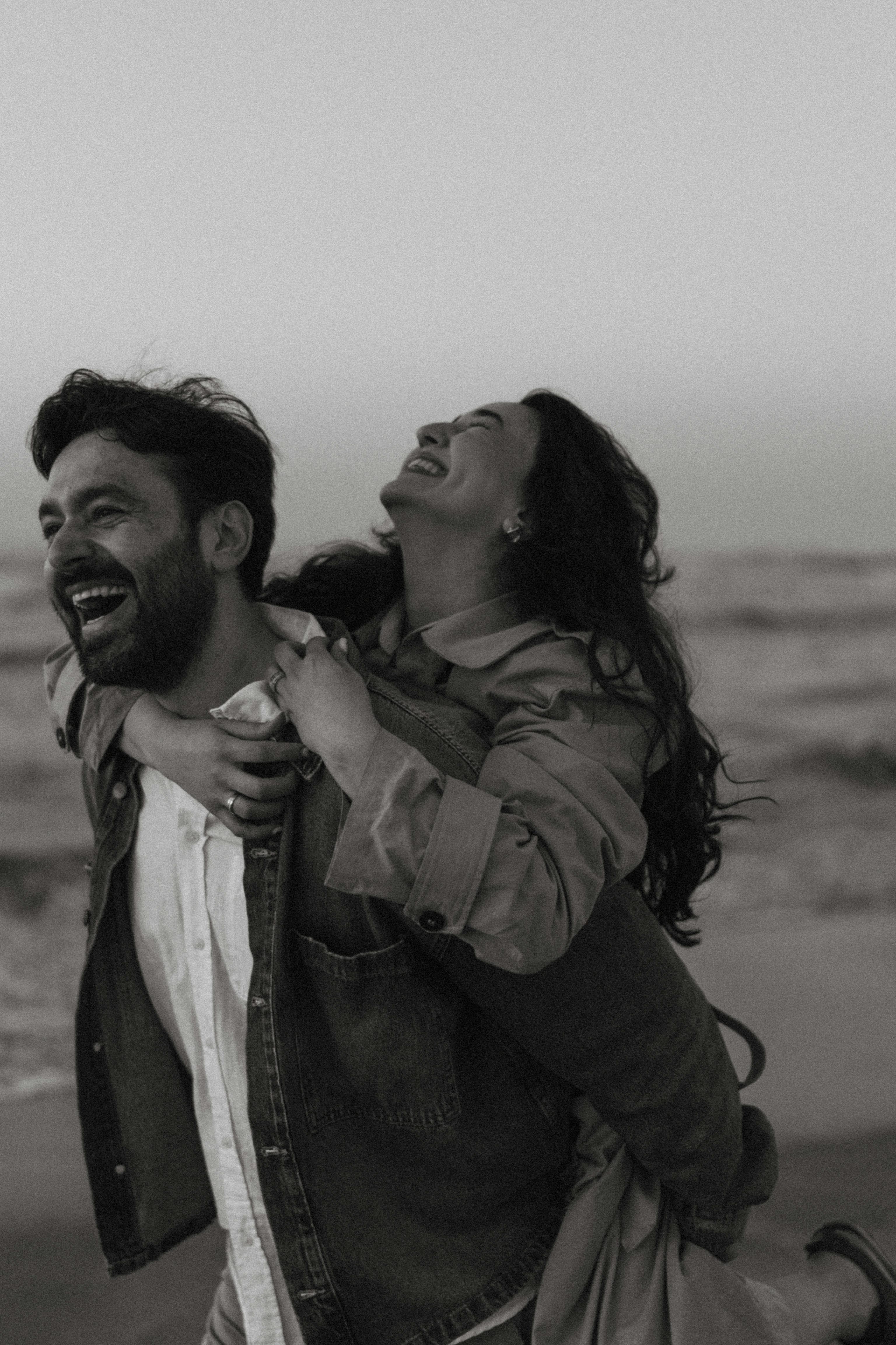 A happy couple enjoying laughter and a piggyback ride on a serene beach day.
