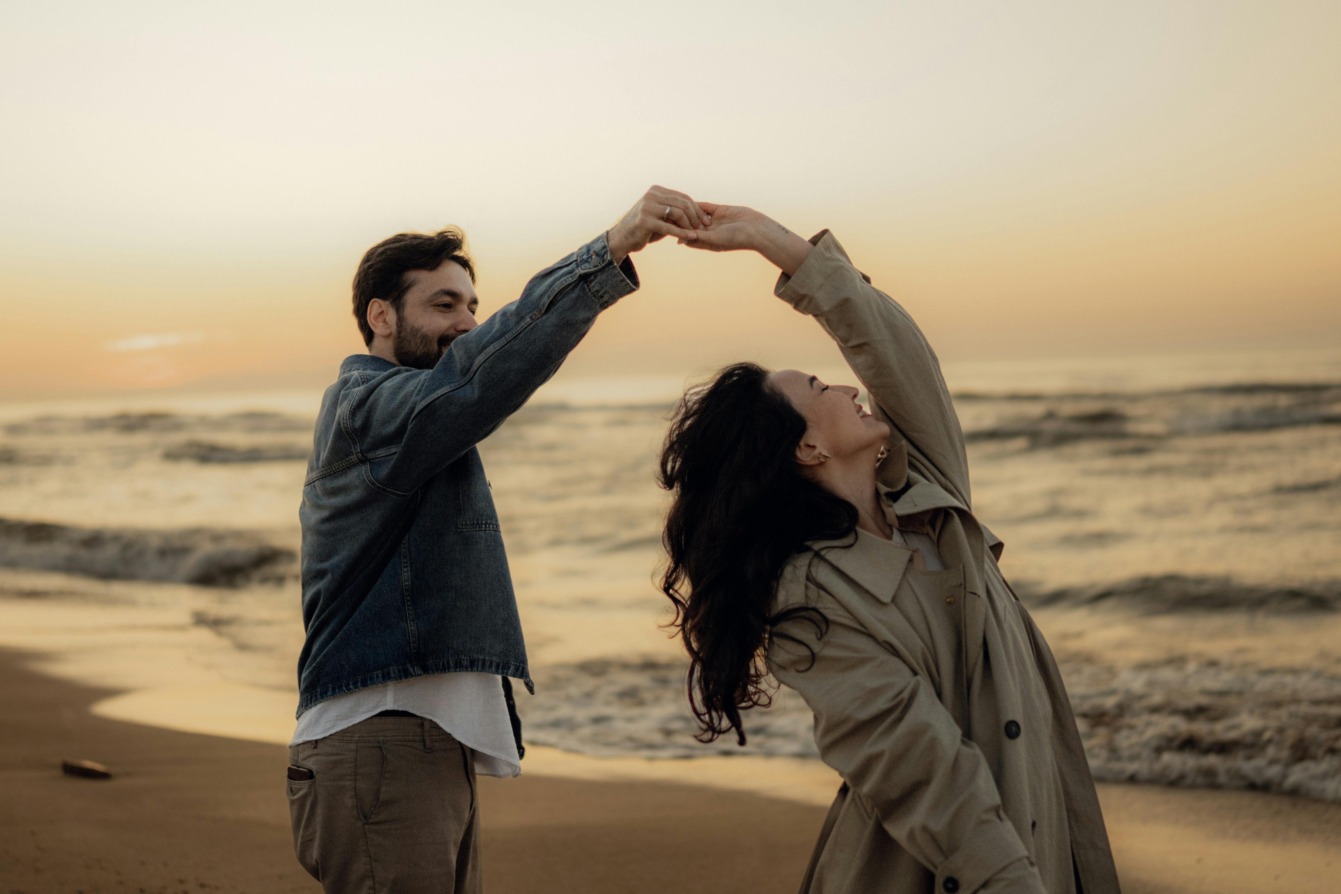 A joyful couple dancing on a beach at sunset, capturing a romantic and carefree moment.
