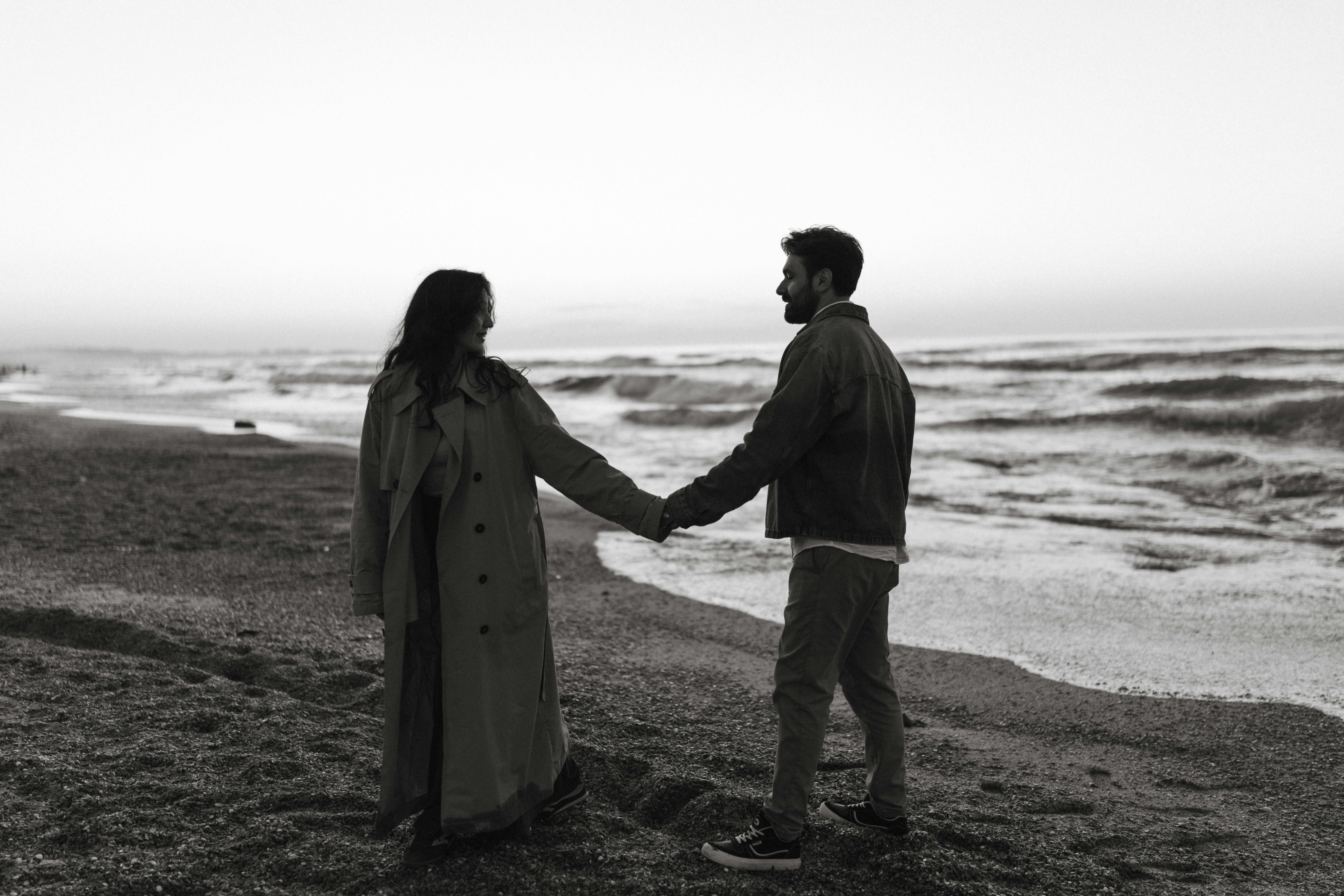 A couple holds hands on a serene beach at twilight, capturing a moment of connection.