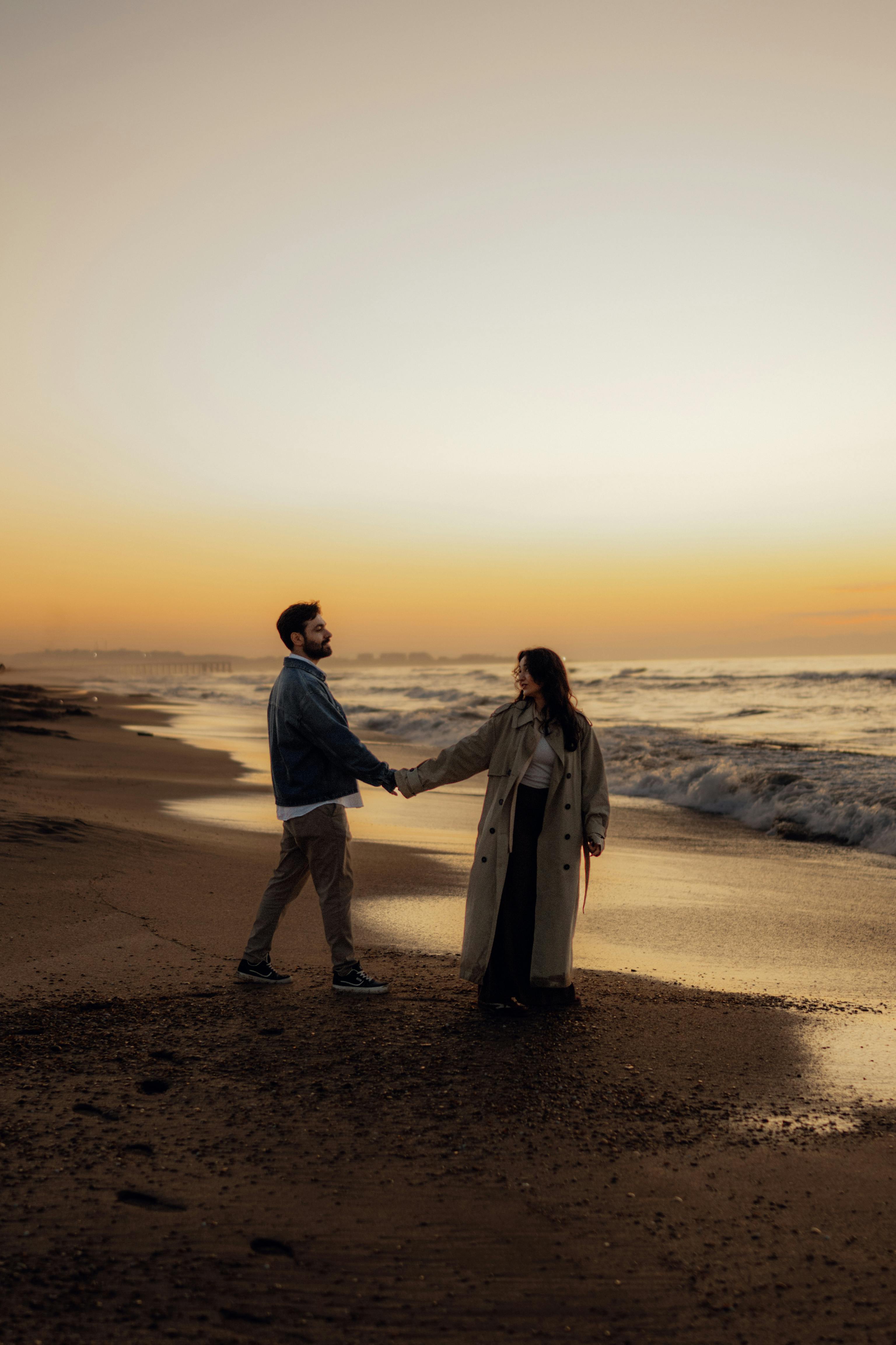 A couple holding hands and walking along a beach at sunset, creating a romantic atmosphere.