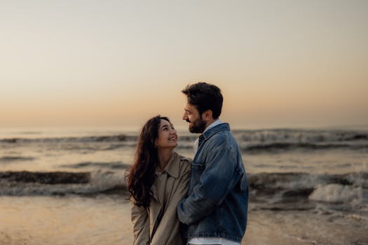 Couple shares a tender moment by the ocean at sunset, evoking warmth and romance.
