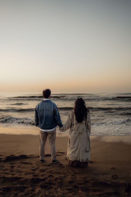 Serene scene of a couple holding hands while facing the ocean at sunset.