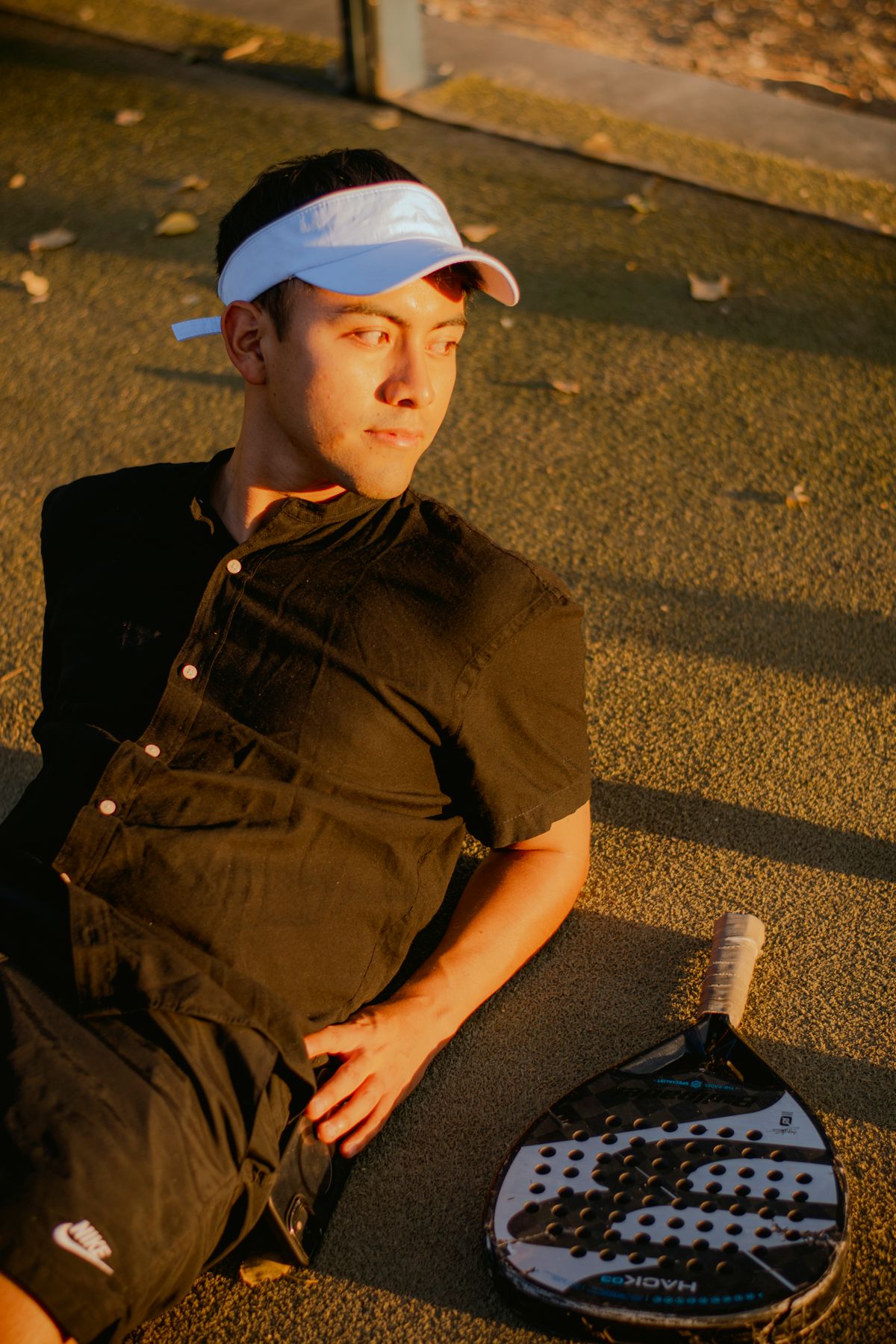 A player in a white visor sits courtside in warm evening light with his racket