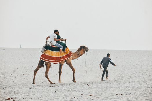 Tourists enjoying a camel ride led by a guide across sandy desert terrain, showcasing adventure and cultural experience.