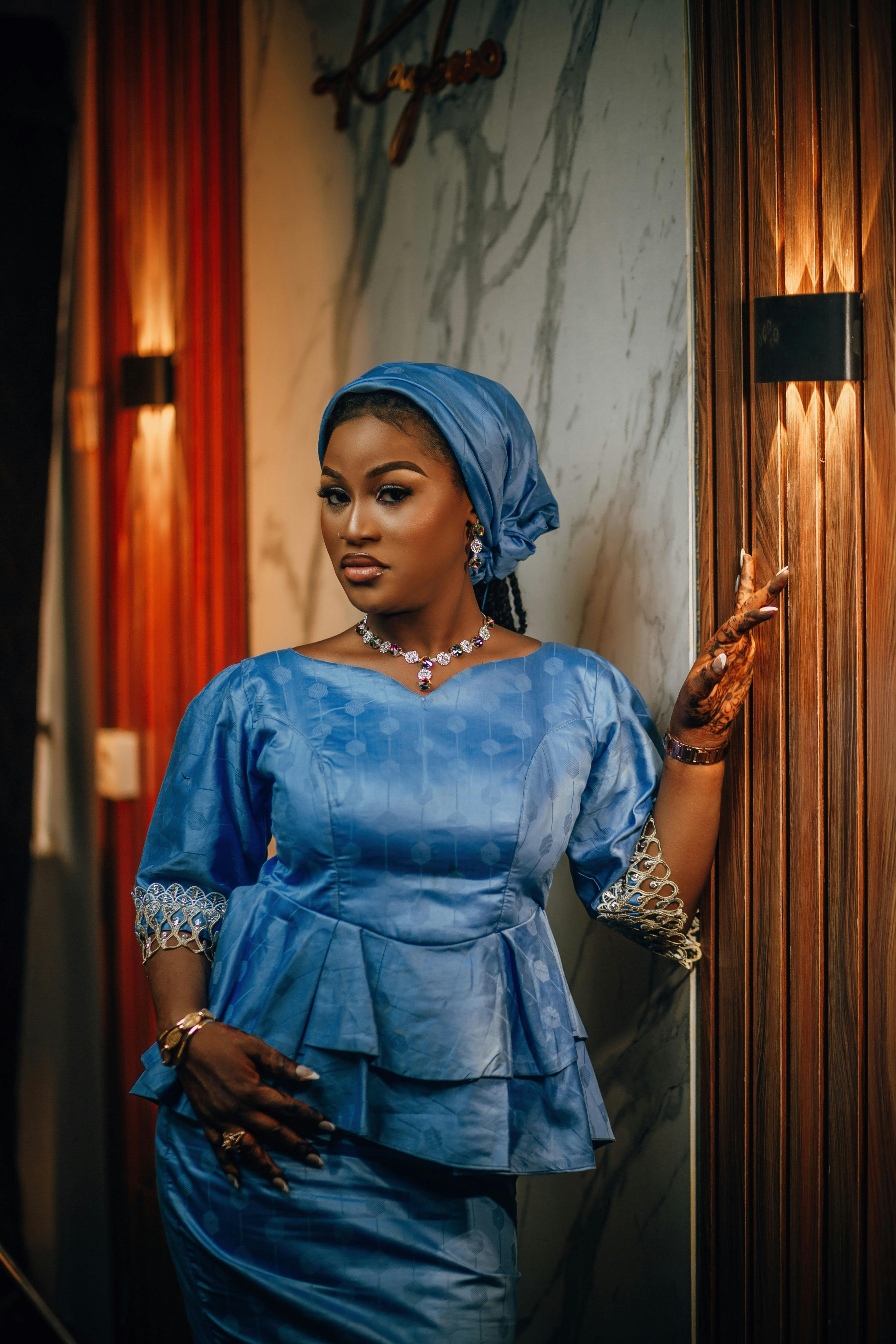 A stylish woman poses gracefully in traditional blue attire indoors, exuding elegance and confidence.