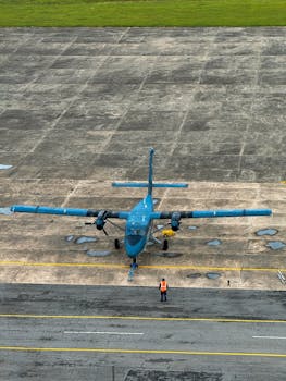 A small blue twin-propeller airplane parked outdoors with a ground crew member visible.
