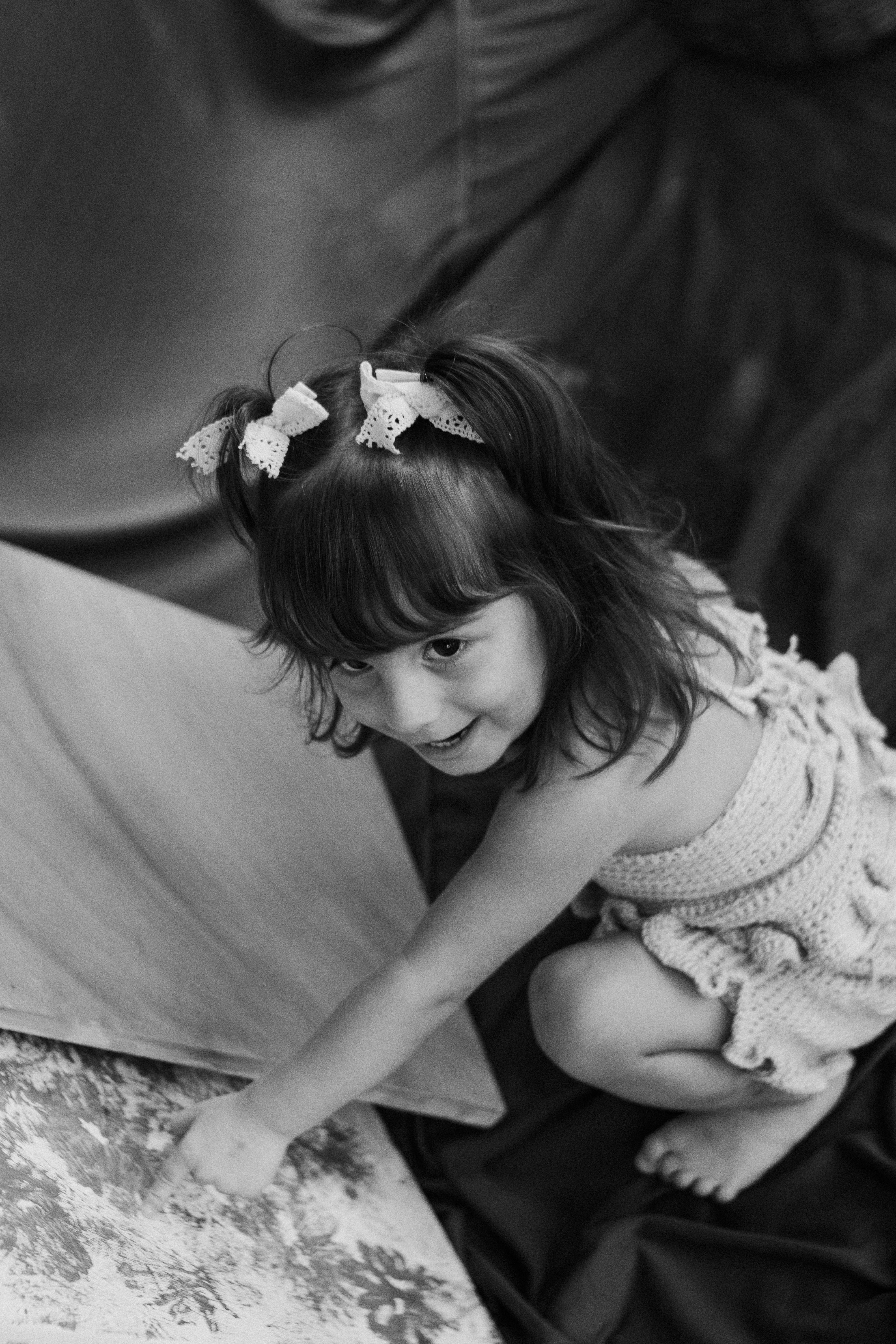 A charming black and white photo of a little girl in a crochet dress indoors with a joyful expression.