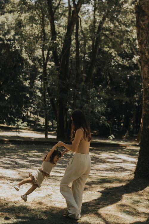 Free A mother spins her child joyfully in a sunlit forest clearing. Stock Photo