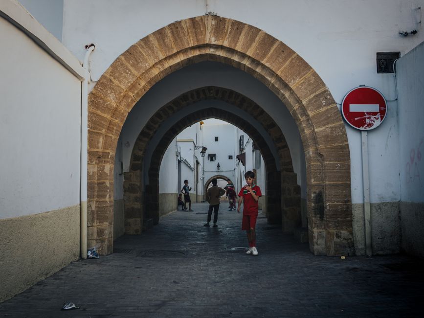 A serene street scene in Rabat, Morocco, featuring an ancient stone archway and pedestrians.