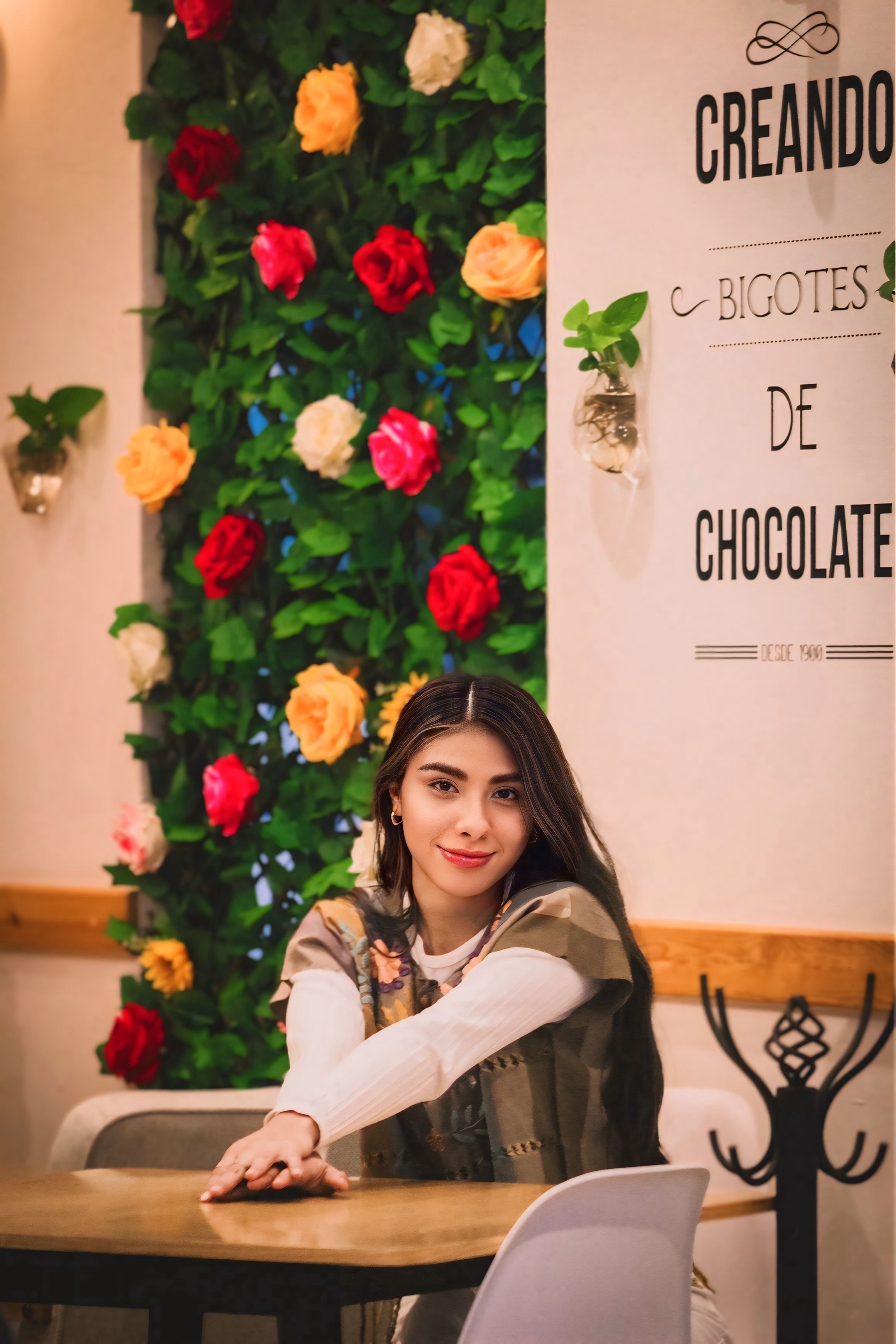 Stylish woman in a cozy cafe with floral backdrop, vibrant and inviting.