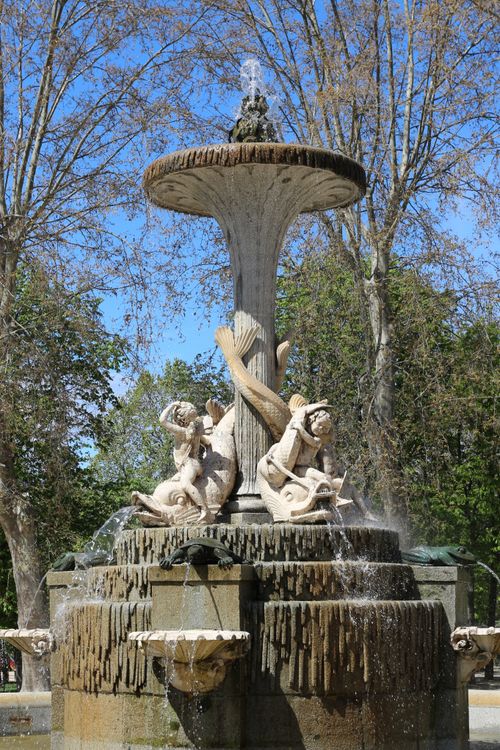 Free Intricate stone fountain with sculptures in a sunlit park surrounded by trees. Stock Photo